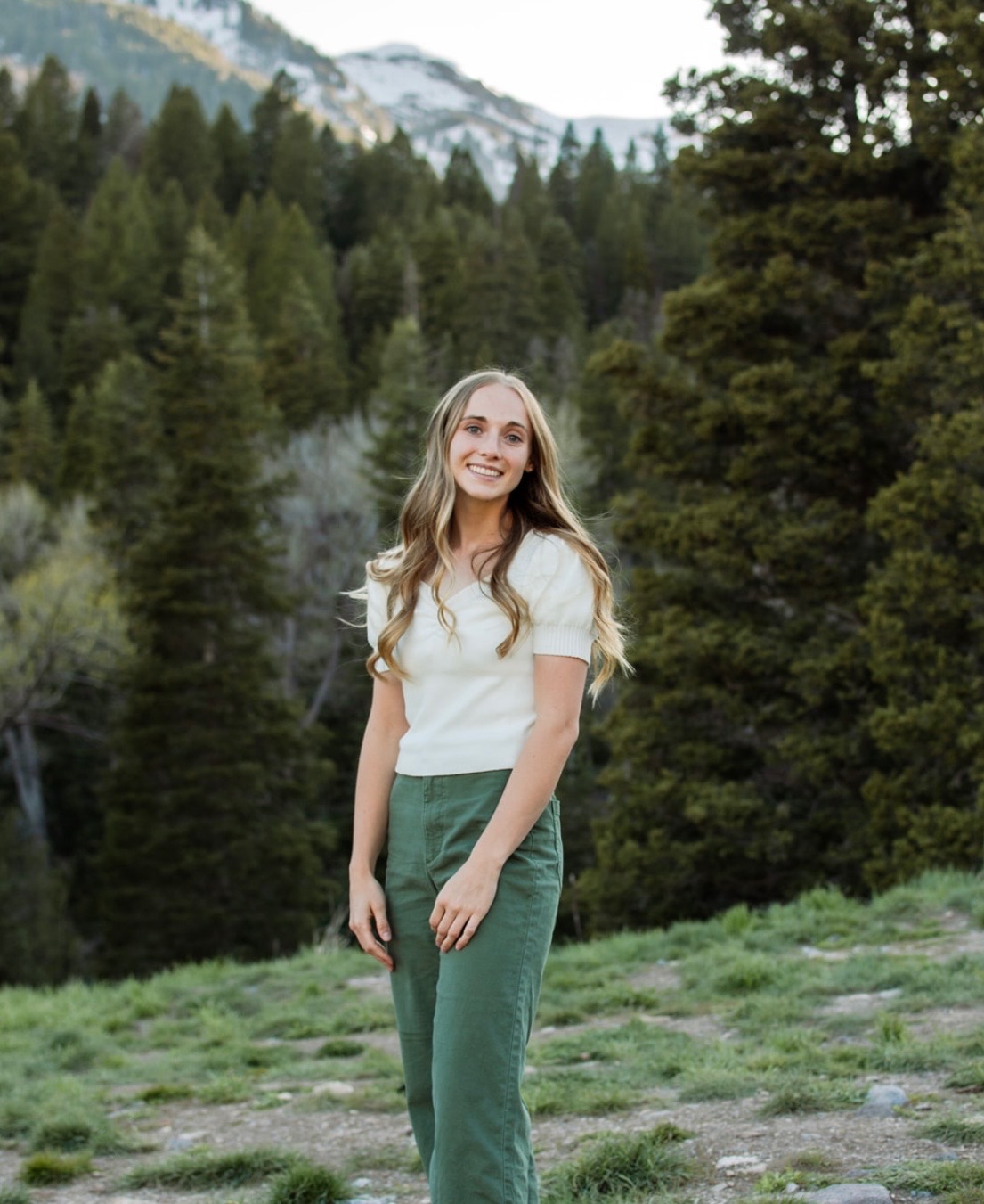 Melody, founder and artist of Everbloom, standing outdoors in front of pine trees and mountains